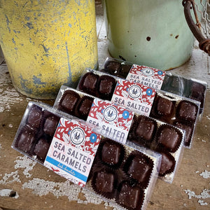 4 boxes of  Salted  Dark Chocolate Caramels on a rustic wood table